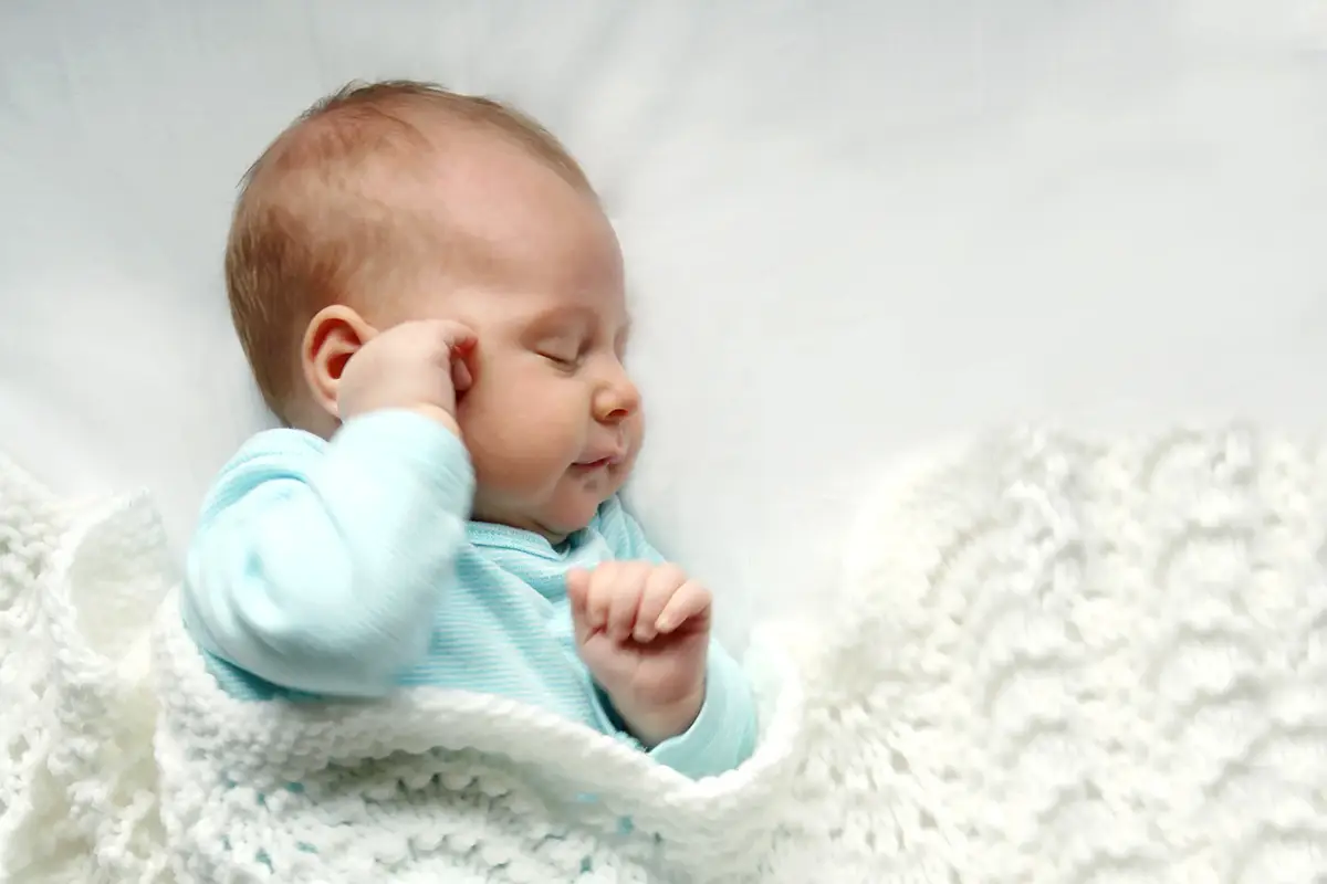 A sweet newborn infant girl is sleeping peacefully while snuggled in warm white blankets
